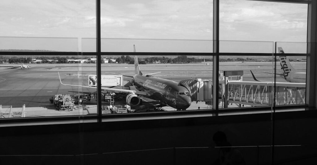 Monochrome view of an airport runway showcasing airplanes and gates through large windows.