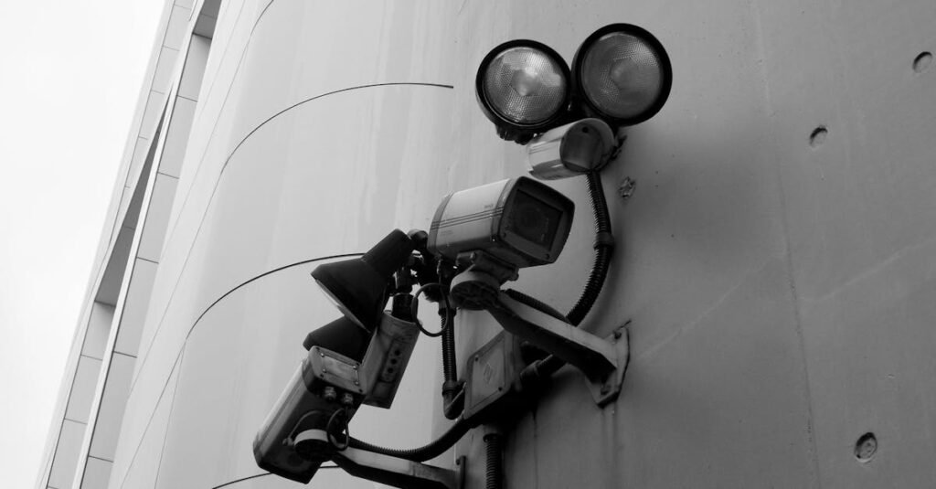 Close-up of a black and white CCTV surveillance camera with spotlights mounted on a building wall.