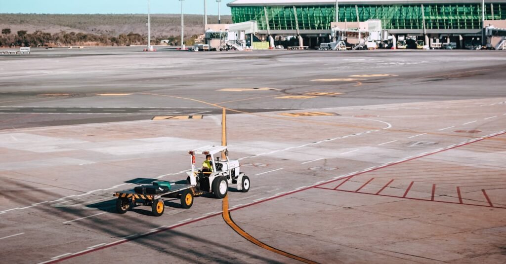 A luggage cart on the airport tarmac near a modern terminal building under clear skies.