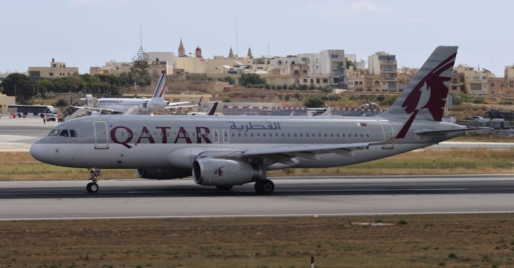 pexels-photo-33052492-33052492 Qatar Airways aircraft taxiing at airport with cityscape in the background.
