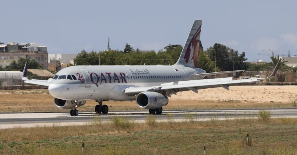 Qatar Airways Airbus A320 taxiing on runway with clear blue sky.