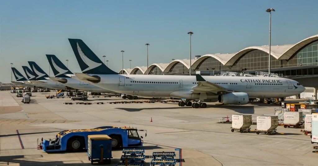 Cathay Pacific aircraft lined up at Hong Kong International Airport apron with cargo vehicles nearby.