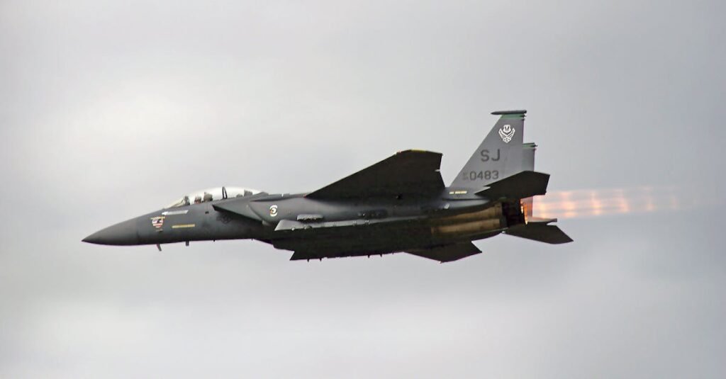 Dramatic view of F-15 fighter jet flying outdoors, showcasing afterburners against a cloudy sky.